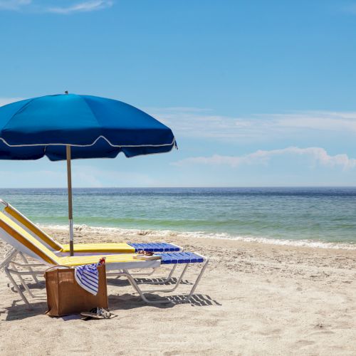 A beach scene with a blue umbrella, sun loungers, and the ocean under a clear sky.