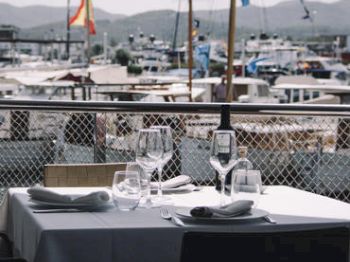 A table set for dining outdoors with boats and flags in the background.