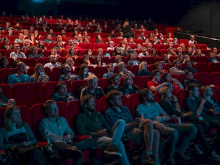 Audience sitting in a theater with red seats, possibly watching a performance or film.