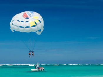 Two people are parasailing above clear blue waters, with a boat beneath them.