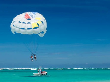 Two people are parasailing above clear blue waters, with a boat beneath them.