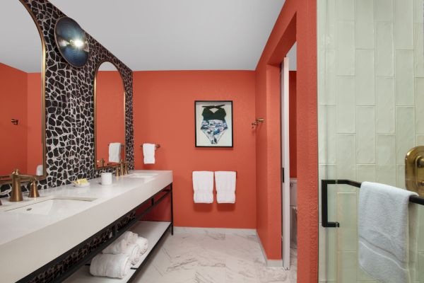 A stylish bathroom with coral walls, a large mirror, and white towels.