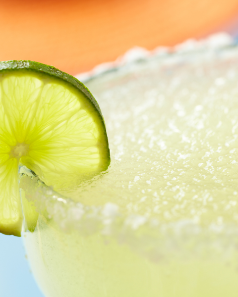 A close-up of a margarita garnished with a lime slice on the rim, featuring a salted edge and a blurred background.