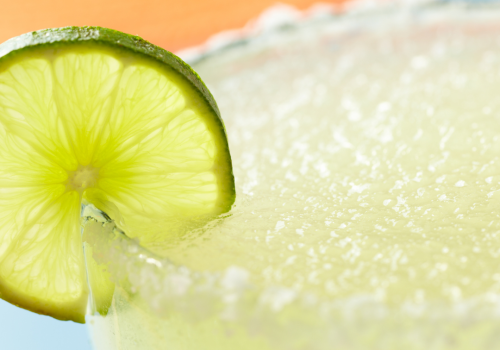 A close-up of a margarita garnished with a lime slice on the rim, featuring a salted edge and a blurred background.