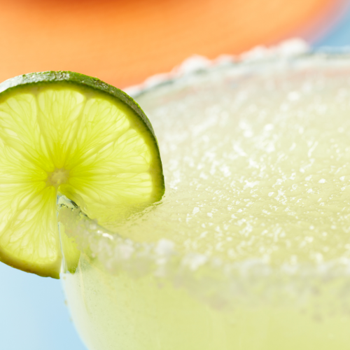 A close-up of a margarita garnished with a lime slice on the rim, featuring a salted edge and a blurred background.