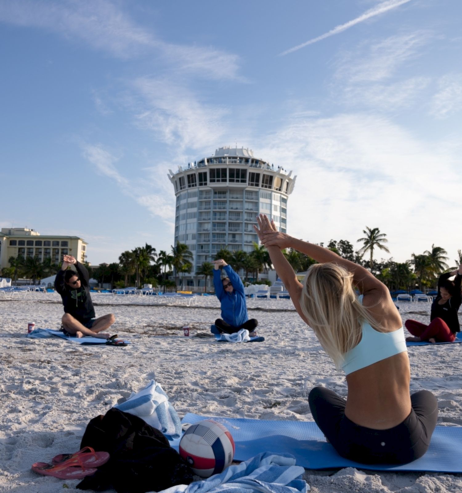 People are practicing yoga on a beach at sunset.