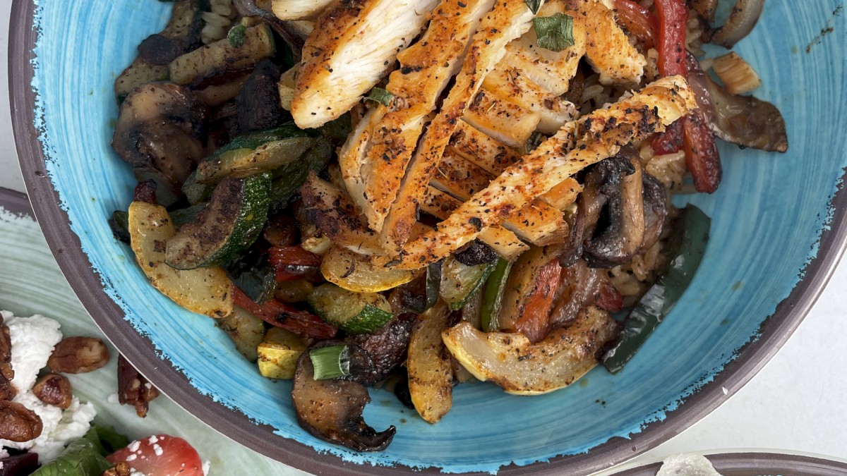 The image shows a bowl with grilled chicken and vegetables, a side salad with strawberries, and a bowl of bread or crackers, ending the sentence.