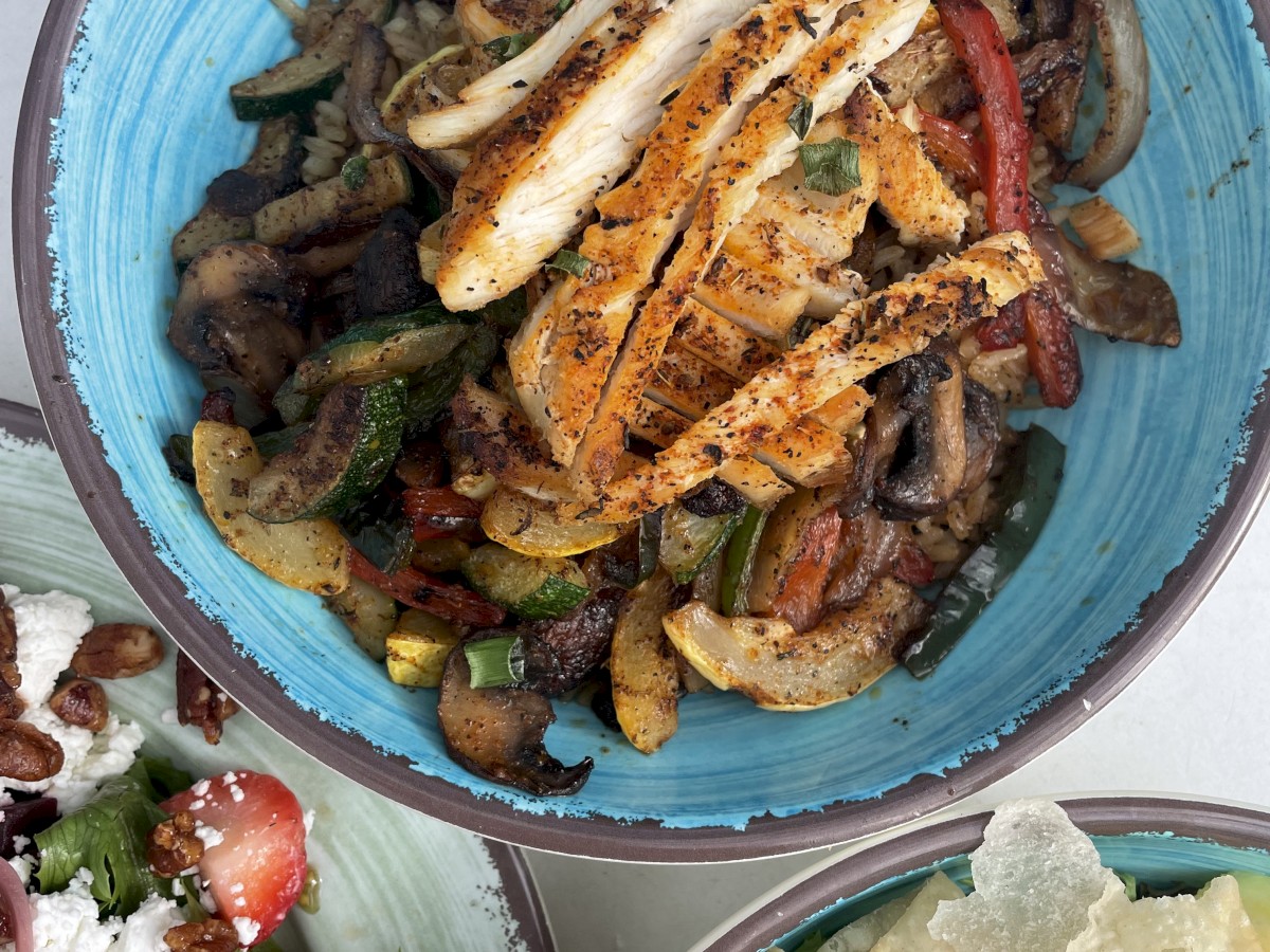 The image shows a bowl with grilled chicken and vegetables, a side salad with strawberries, and a bowl of bread or crackers, ending the sentence.