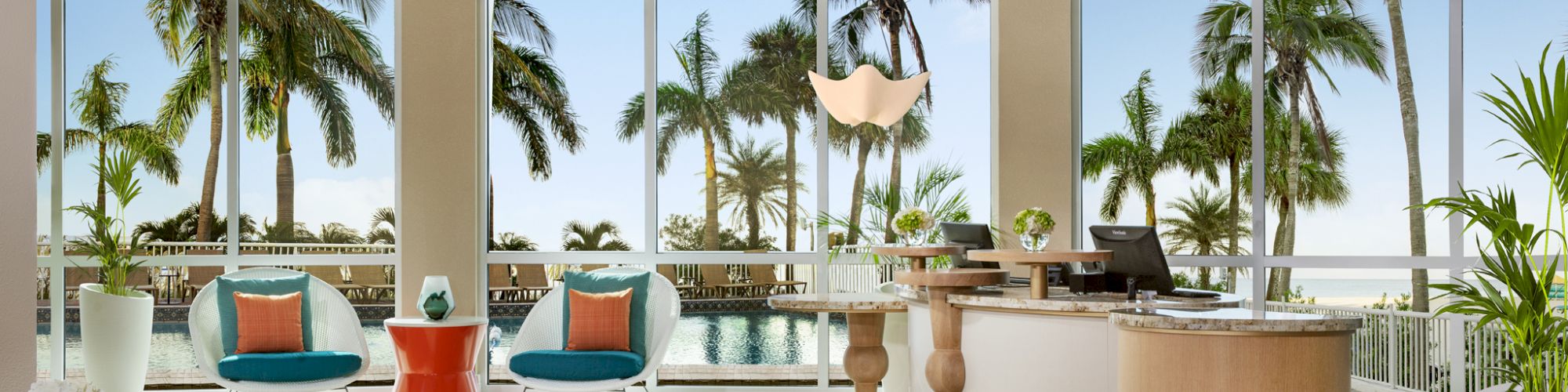 A modern lobby with a reception desk, stylish seating, large windows showcasing palm trees, and a pool area outside ends the sentence.