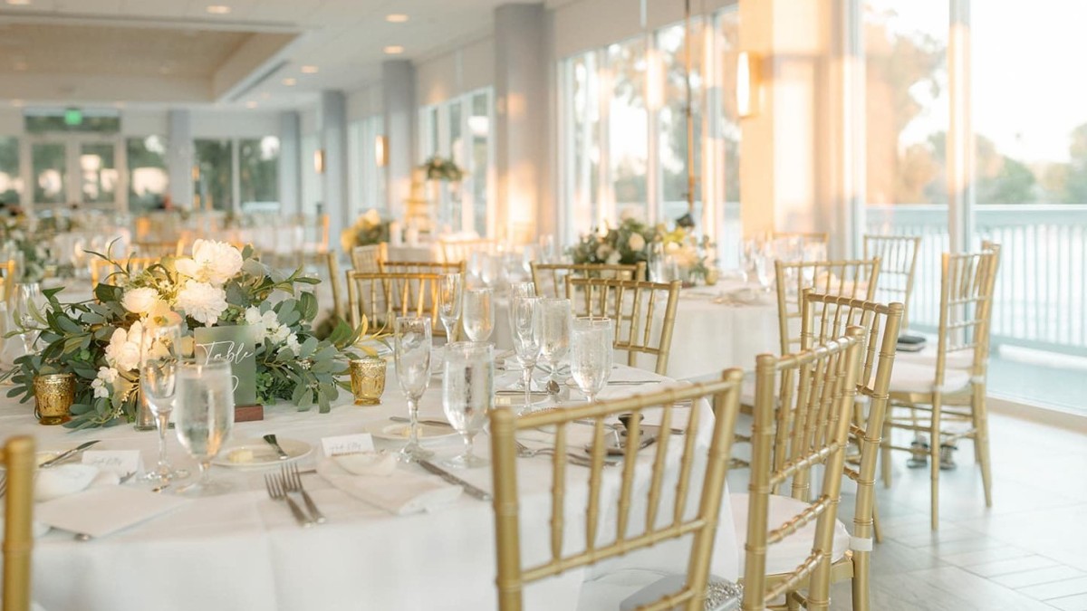 Elegant dining setup with gold chairs and white floral centerpieces.