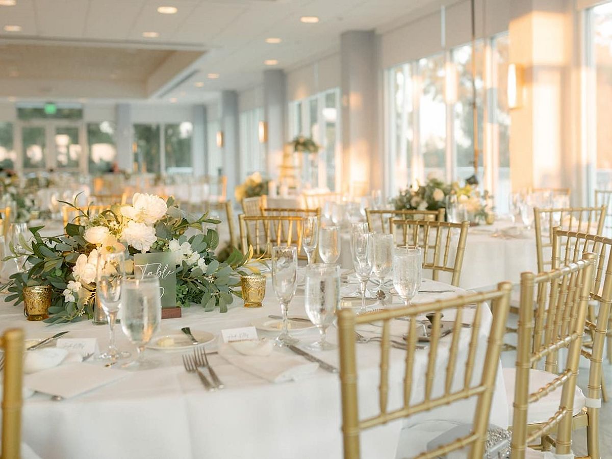 Elegant dining setup with gold chairs and white floral centerpieces.