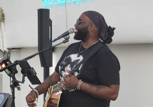 A man is playing the guitar and singing into a microphone. Above him is a neon sign that reads, 