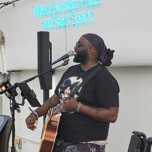 A man is playing the guitar and singing into a microphone. Above him is a neon sign that reads, 