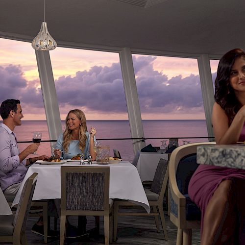 A couple is dining at a restaurant with scenic ocean views, while a woman in a purple dress enjoys a drink at the bar, all during sunset.