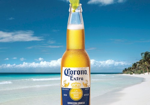 A Corona Extra beer bottle with a lime wedge in the neck is placed on a rock at a beach featuring clear water, white sand, and a blue sky.