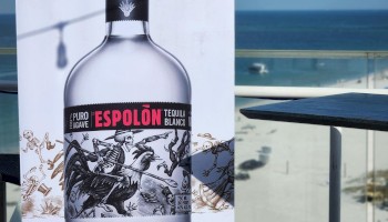 Banner of Espolon Tequila with bottle image, beach view in background, white cooler with items including hats, on a balcony.