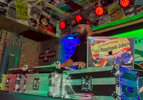 A DJ is performing in a colorful, poster-filled room with equipment and a visible sign reading 