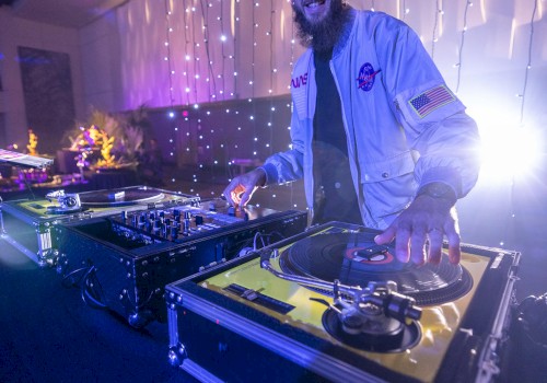 A DJ is performing on a set of turntables in a dimly lit room with string lights in the background and a relaxed atmosphere.