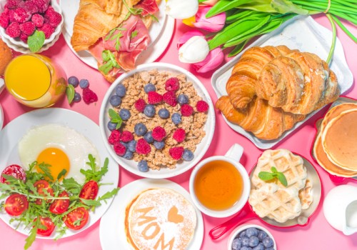 The image features a breakfast spread with croissants, a fried egg, cereal with berries, pancakes, waffles, coffee, juice, and a floral bouquet.