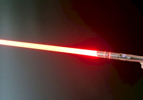 A hand holding a realistic red lightsaber with an illuminated blade, resembling a weapon from a popular sci-fi franchise.