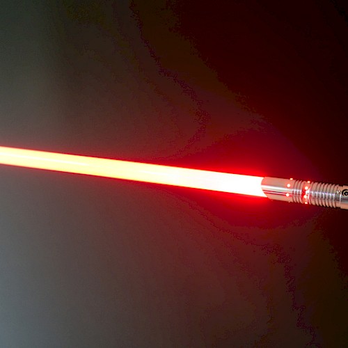 A hand holding a realistic red lightsaber with an illuminated blade, resembling a weapon from a popular sci-fi franchise.