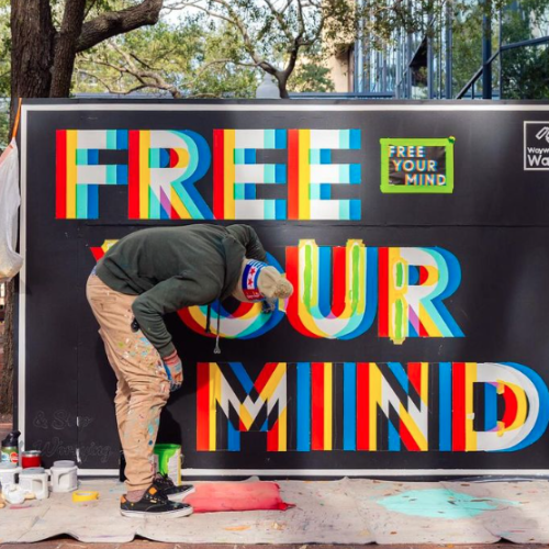 A man is painting a colorful sign on a black background that reads 