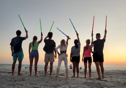 Group of people holding  lightsabers on the beach at sunset.