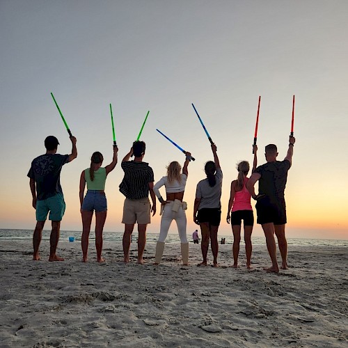 Group of people holding  lightsabers on the beach at sunset.